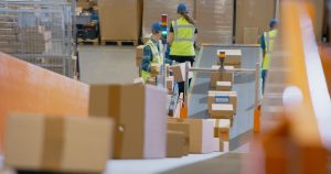 Boxes on conveyor belt in warehouse with workers filling orders for outsourced fulfilment. 