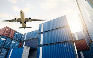 Cargo plane flying over containers being moved for air freight and fulfilment.