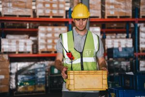 Racked pallet storage behind a warehouse worker moving a carton for fulfilment.