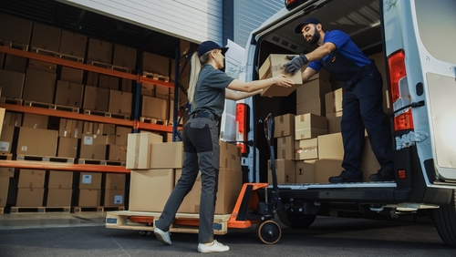 3PL in England with workers moving parcels onto a van for fulfilment at loading dock. 