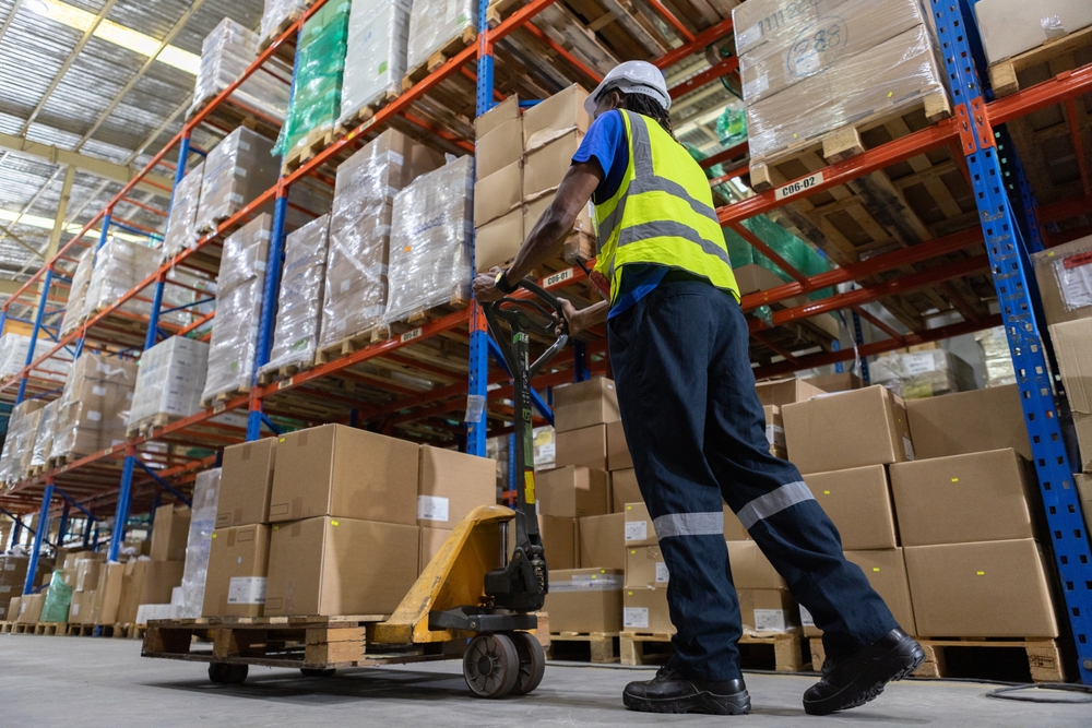 Warehouse worker pushing pallet storage on pump truck down aisle in Altrincham.
