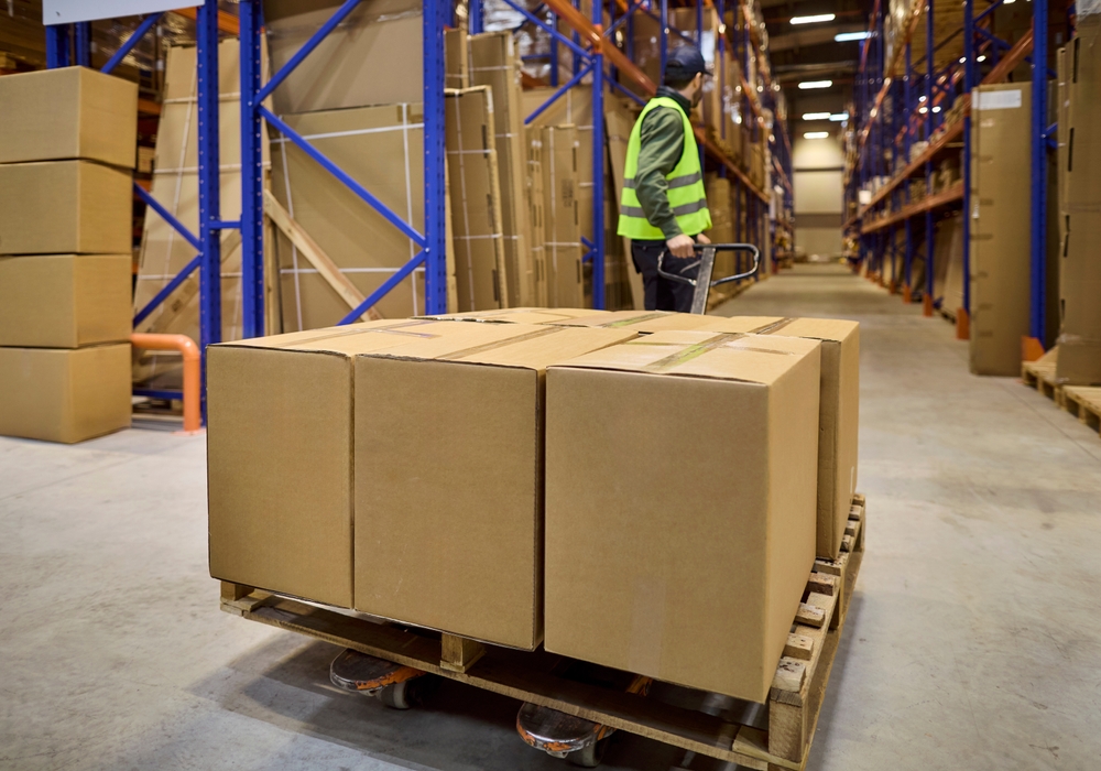 Warehouse worker moving pallet with boxes with a pump truck into storage and ready for logistics. 