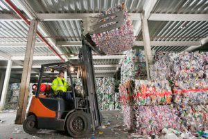 Forklift operator moving bales of plastic within a warehouse. 