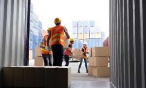 Warehouse workers moving cartons of cardborad boxes out of a container.