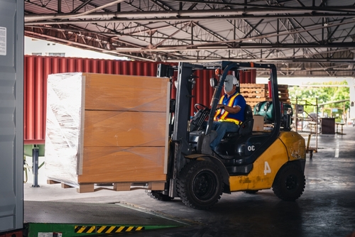 Forklift moving pallets of a container for receipt.