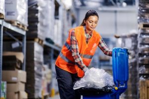 Warehouse worker recycling plastic in blue bins while packaging stock for fulfilment.